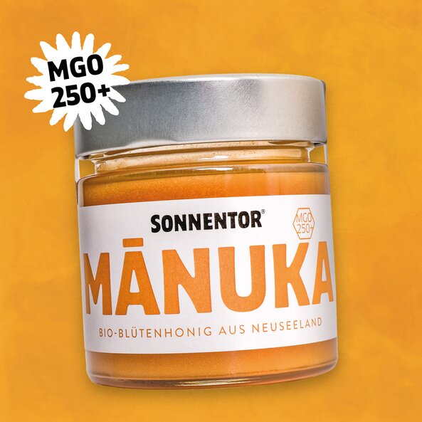 SONNENTOR MÁNUKA Bio-Blütenhonig aus Neuseeland im Glas mit silbernem Deckel und dem Icon "MGO 250+" auf orangem Hintergrund.